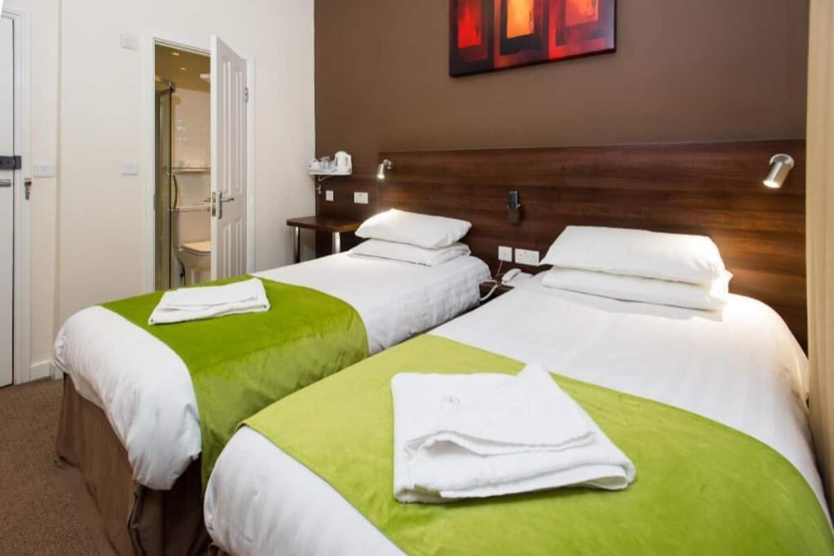 A hotel room with two beds, a shower, and a wall-mounted artwork.