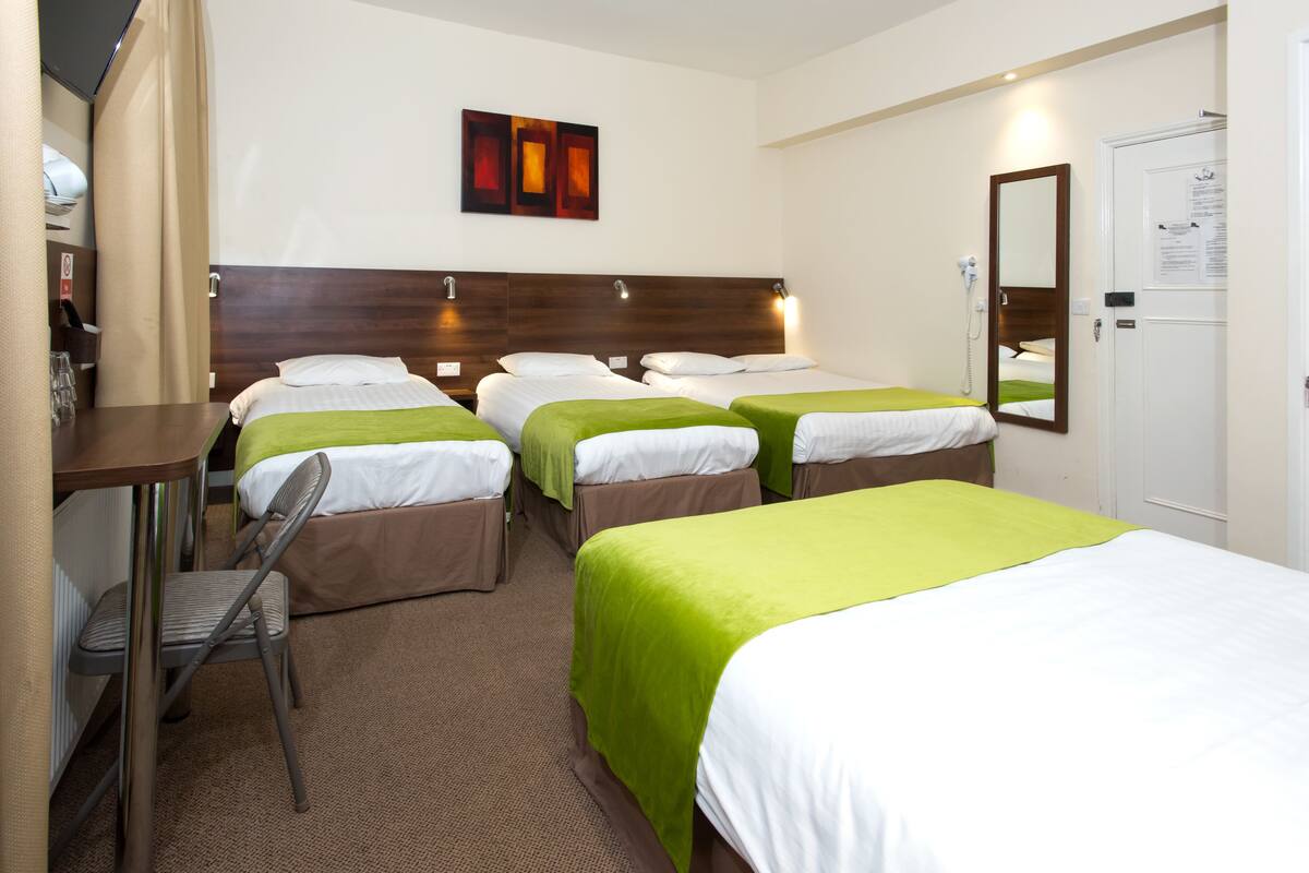 A hotel room with four single beds, a desk with a chair, a mirror, and a door with a notice.