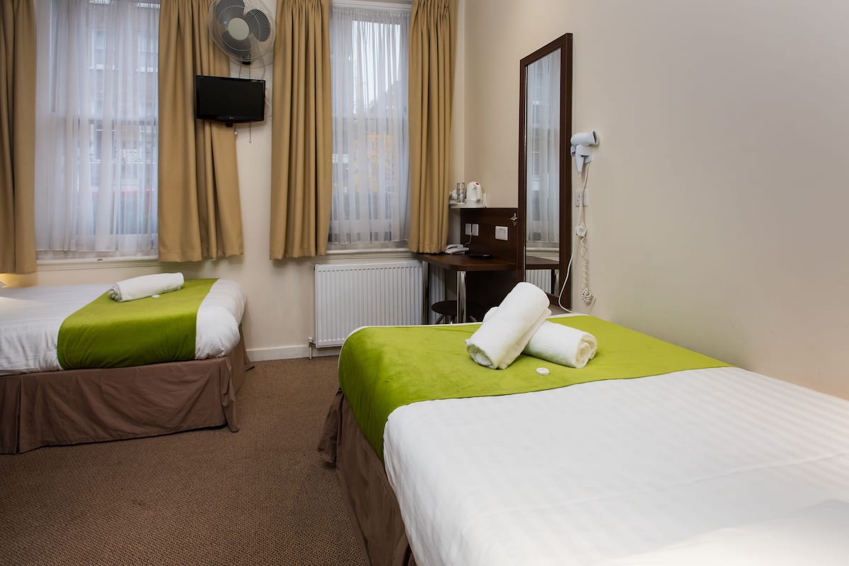 A hotel room with two beds, a desk, a chair, a mirror, a TV, and a window with curtains.