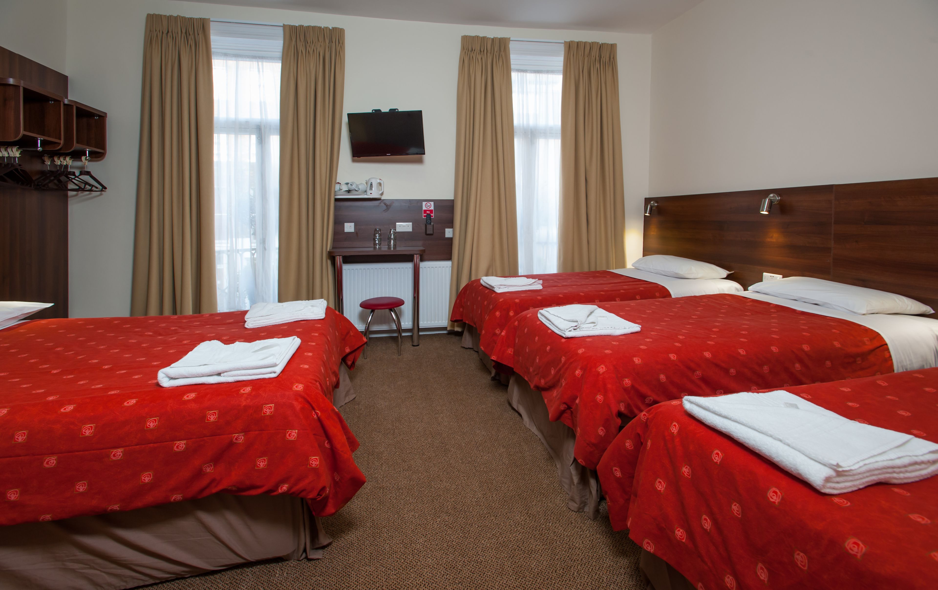 A hotel room with four beds, a desk, a TV, and a coat rack.