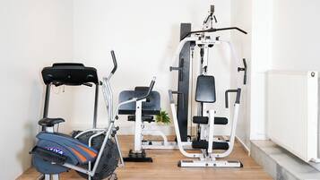 A home gym with an elliptical, a bench press, and a cable machine.
