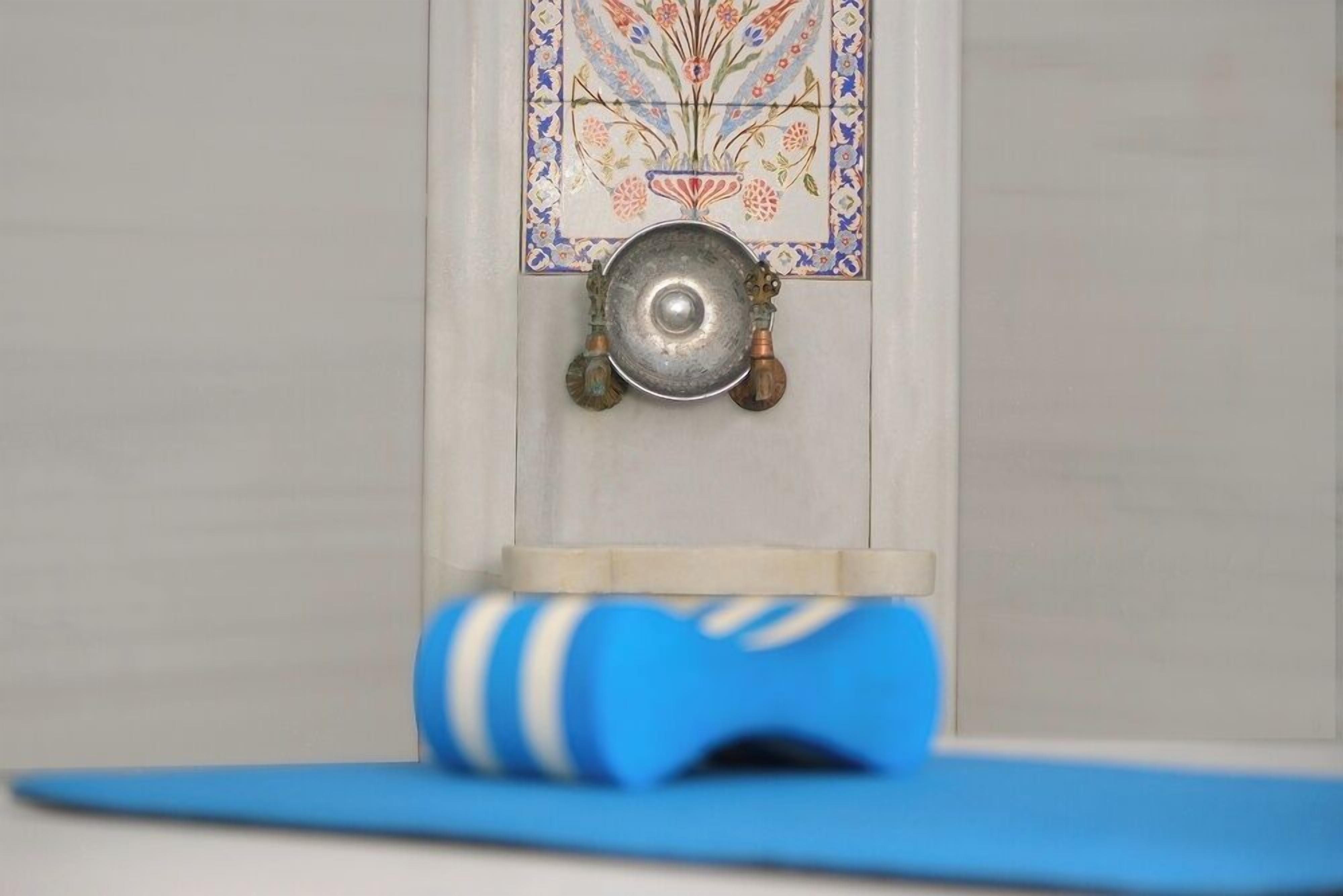 A blue yoga mat on a white floor, a decorative tile with a floral pattern, and a metal bowl hanging on a wall.