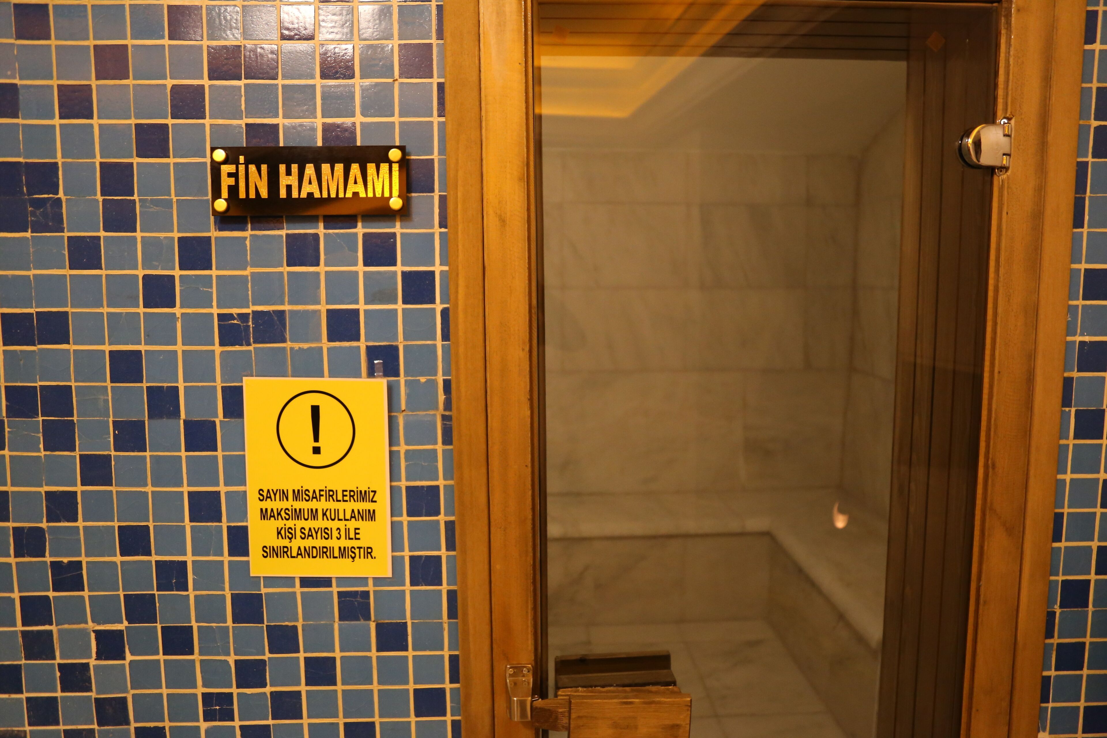Une salle de bain avec un mur carrelé, une porte en bois et un panneau indiquant le nombre maximal de serviettes autorisées.