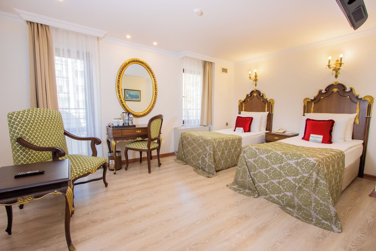 Habitación de hotel con dos camas, un escritorio con una silla, un espejo grande y un televisor.