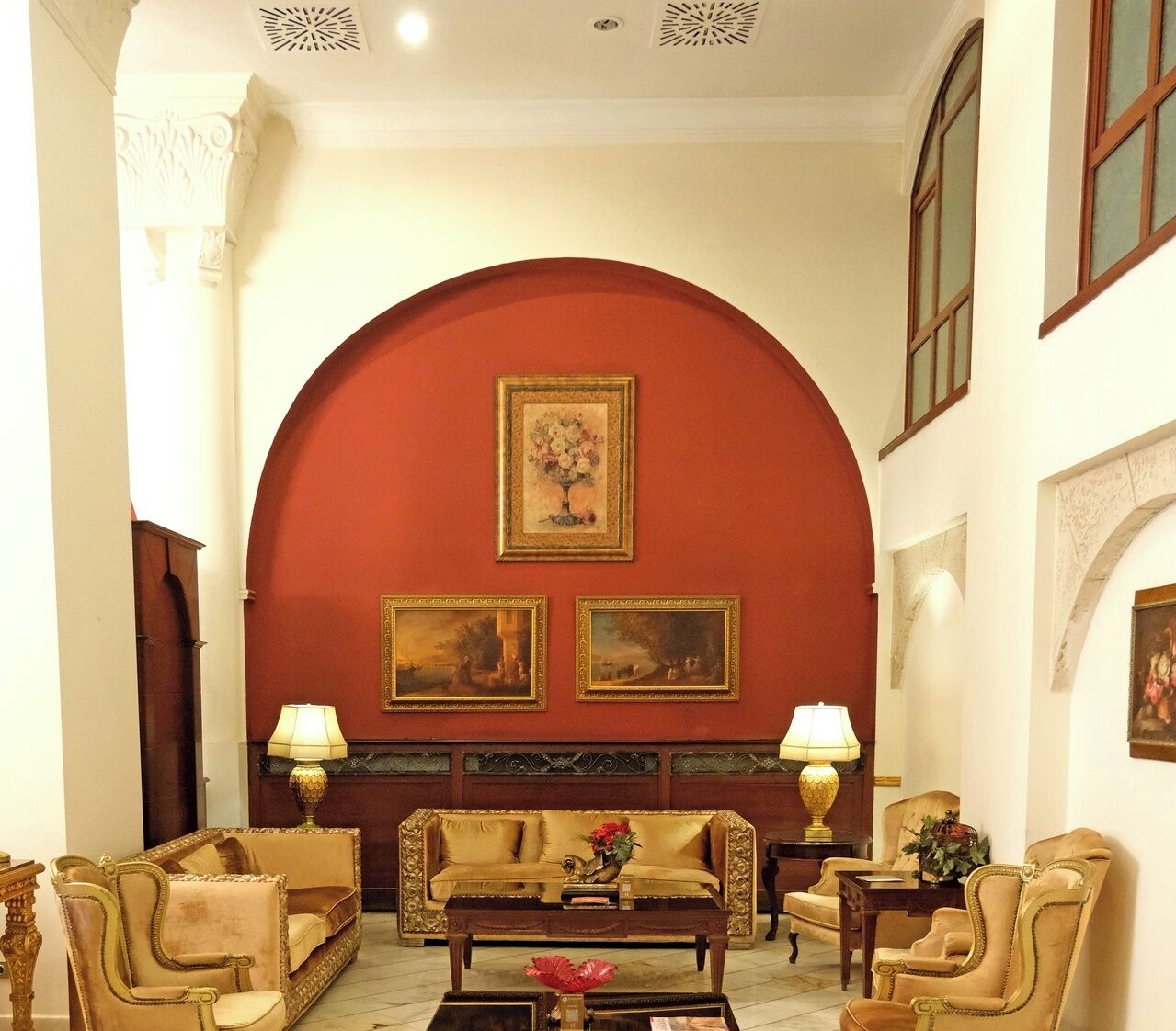 A room with a red archway, two sofas, two armchairs, a coffee table, and two lamps.