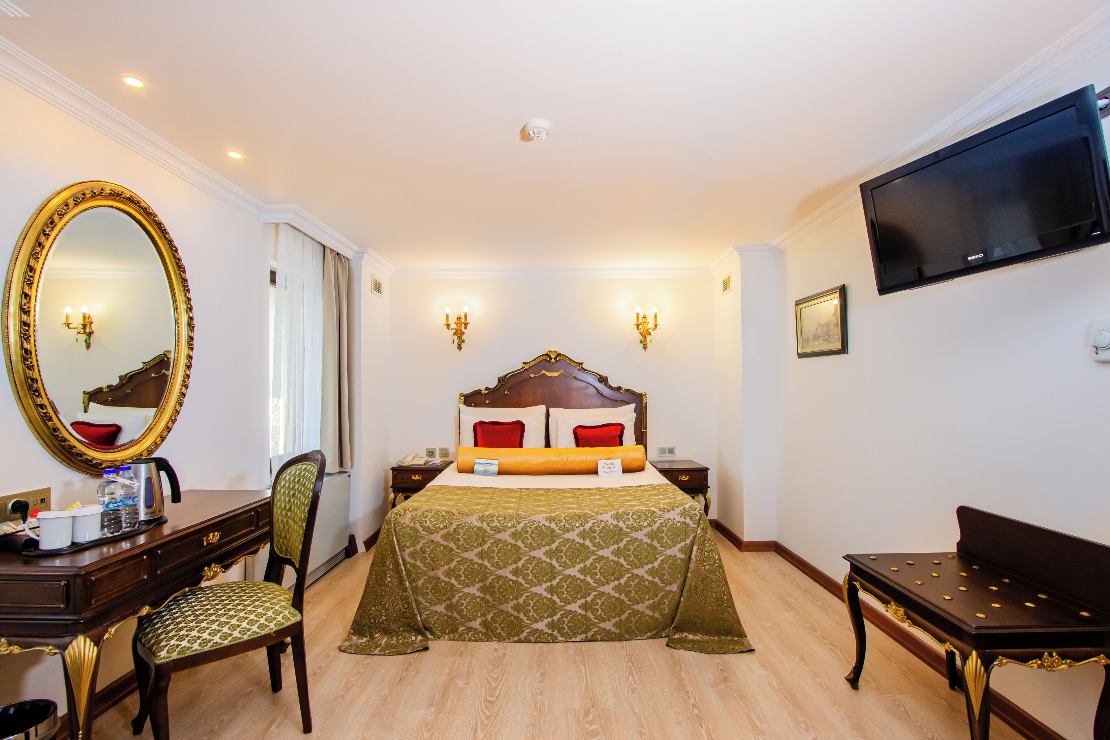 A hotel room with a large bed, a desk with a chair, a television mounted on the wall, and a mirror with an ornate frame.