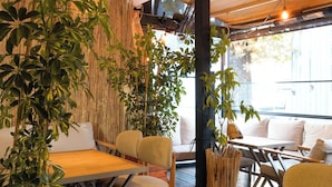 Un espace intérieur accueillant, avec des tables et des chaises en bois, entouré de murs en bambou et agrémenté de plantes en pot.