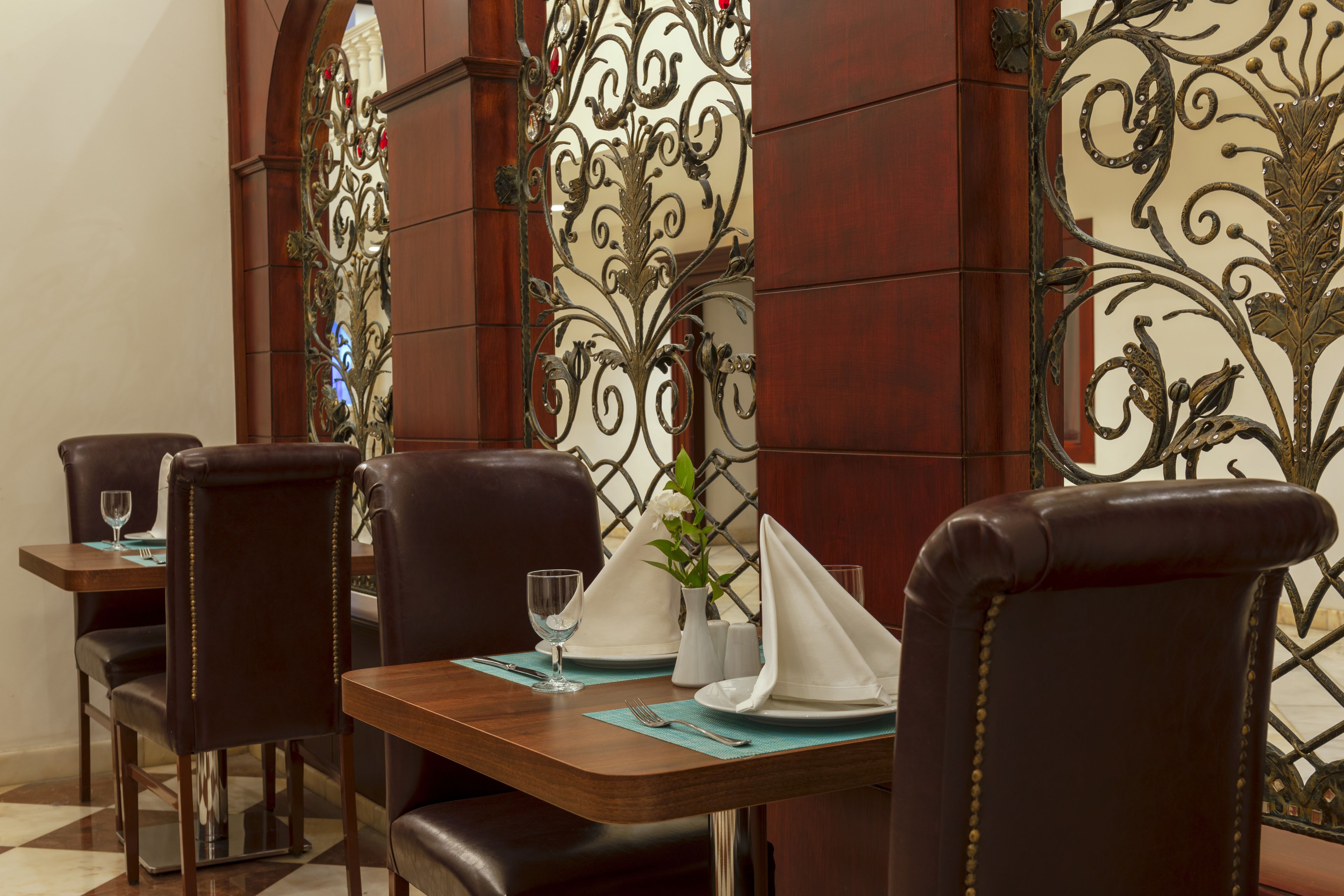 Un comedor con una mesa dispuesta para dos personas, que incluye un florero con flores, una servilleta doblada y un vaso de agua.