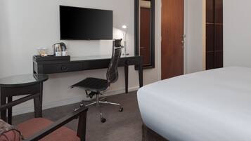 Ein Hotelzimmer mit Bett, Schreibtisch mit Stuhl, Fernseher, Spiegel und Kleiderschrank.