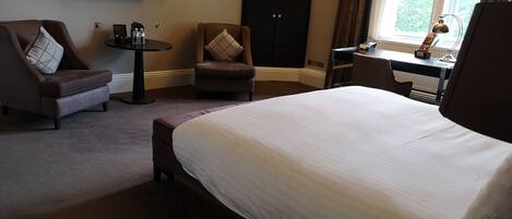 A hotel room with a large bed, a desk, a chair, and a TV mounted on the wall.