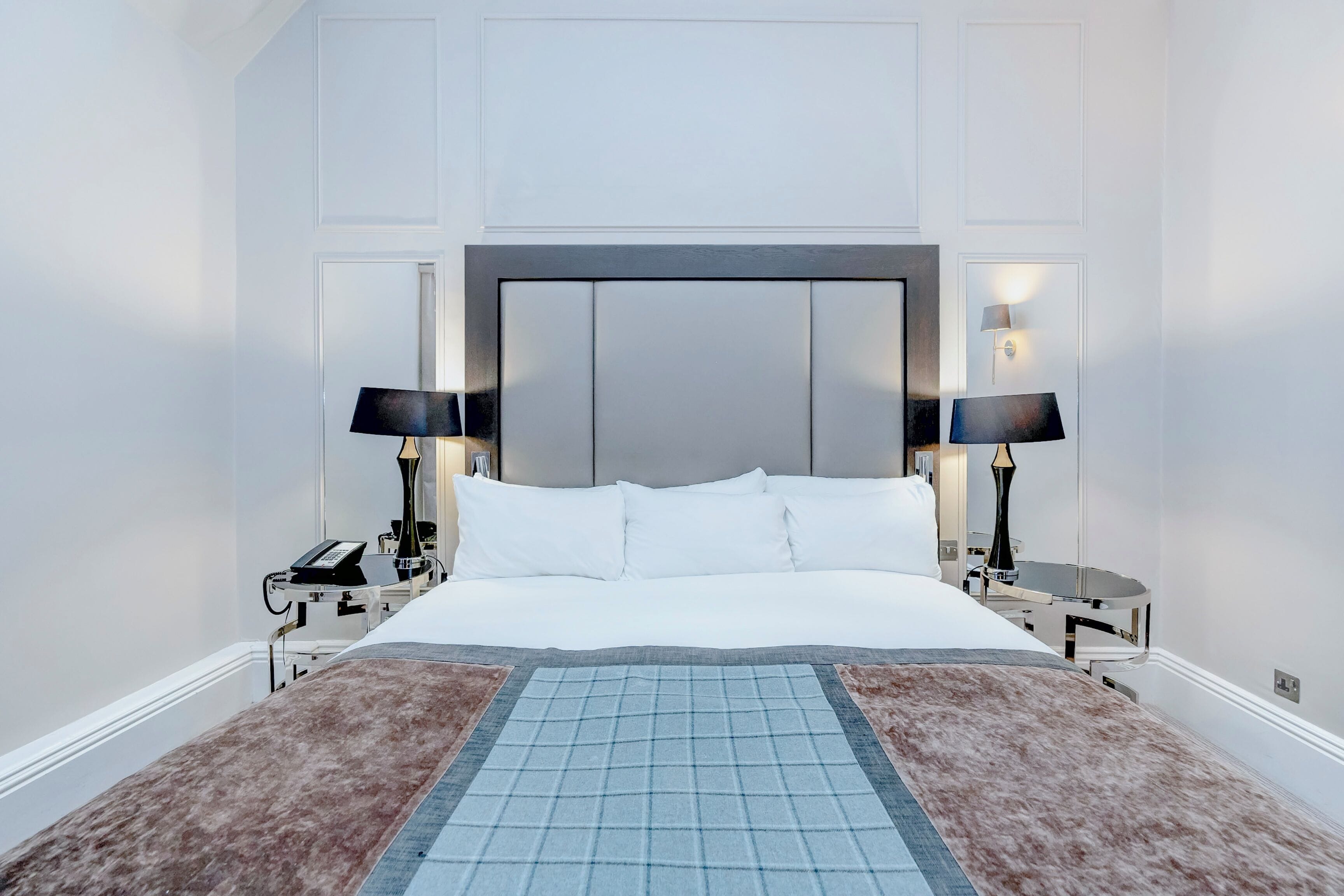 A hotel room with a large bed, two bedside tables with lamps, a telephone, and a decorative rug.