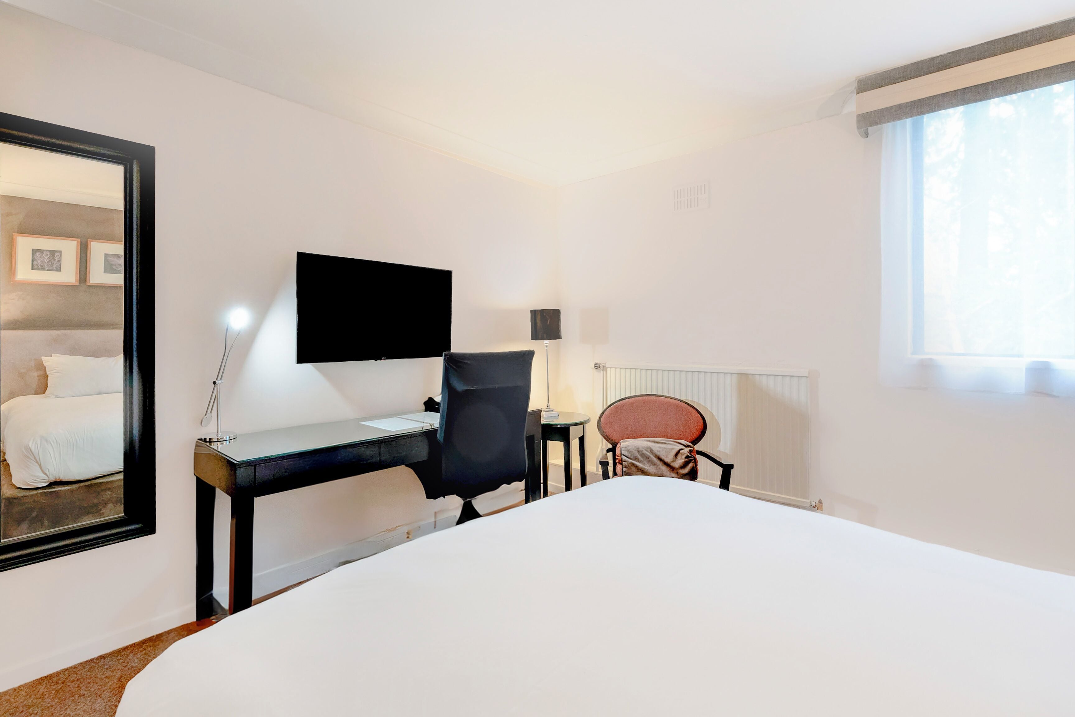 Une chambre d’hôtel avec un lit, un bureau, une chaise, une télévision, une lampe et une fenêtre.
