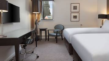 Habitación de hotel con cama, escritorio, silla, televisor y ventana con cortinas.