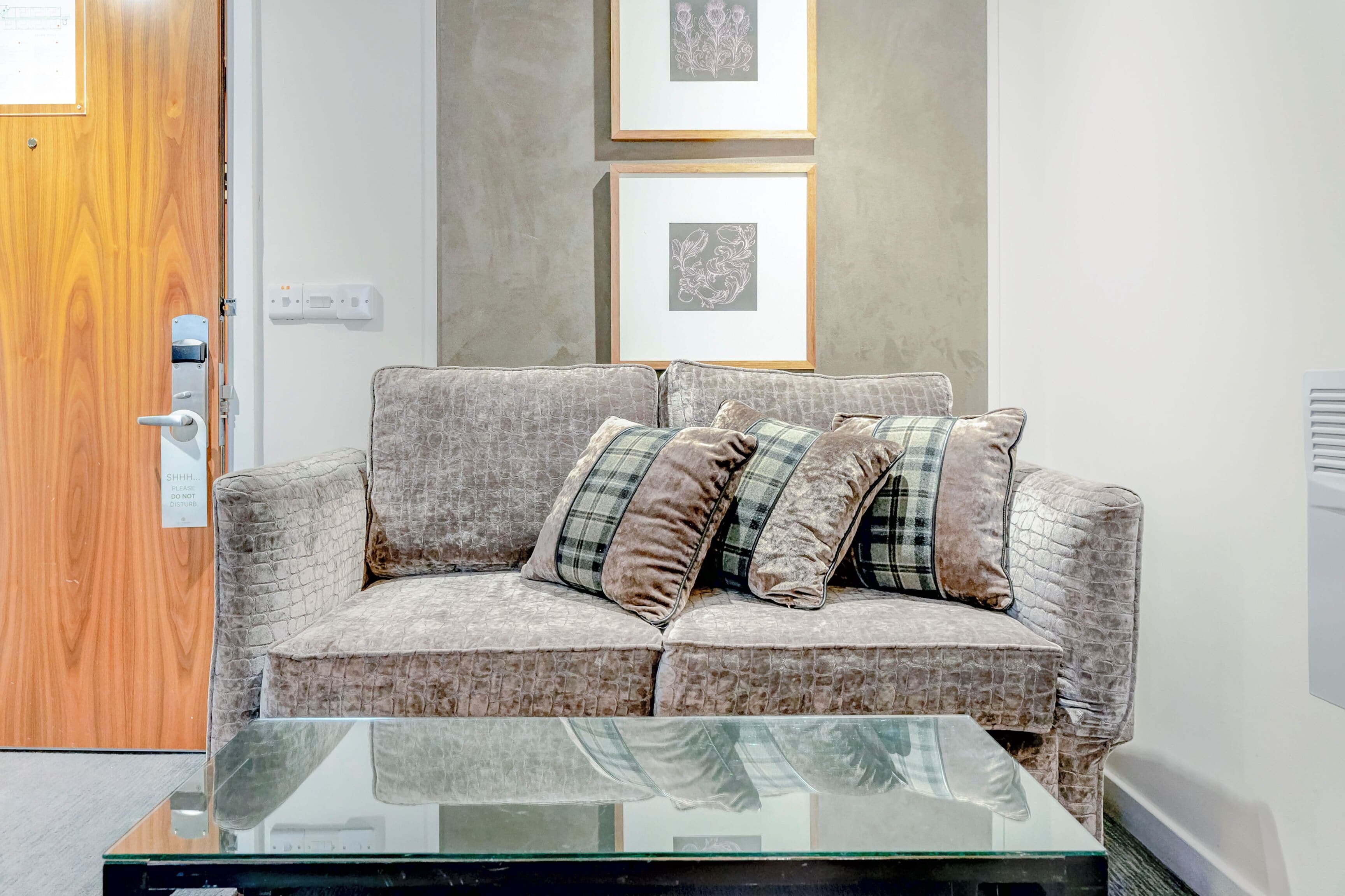 A modern living room with a grey patterned sofa, plaid cushions, and a glass coffee table.
