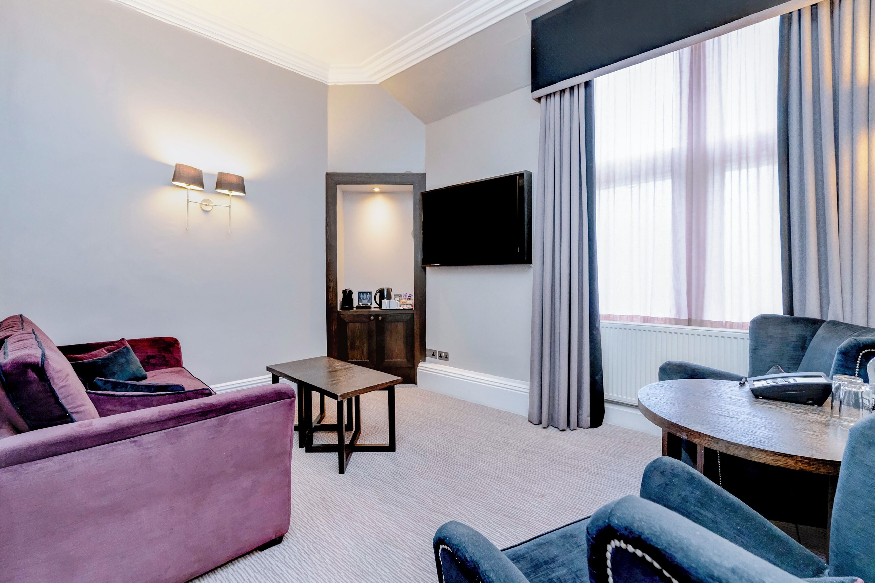 A modern hotel room with a sofa, a round table, a flat-screen TV, and a view of the outdoors.