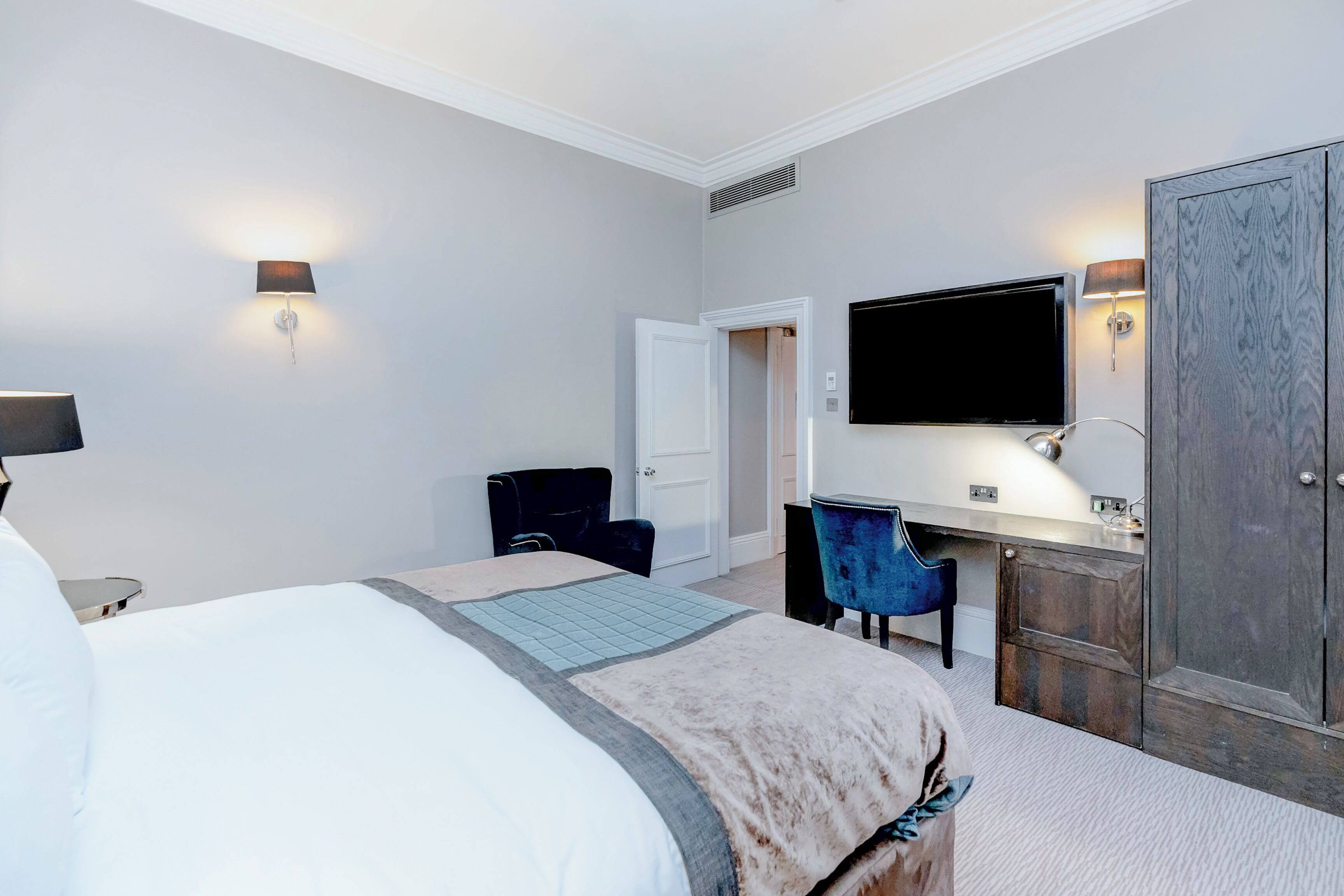 Una camera d'albergo con un letto grande, una scrivania con una sedia, una televisione e un armadio.