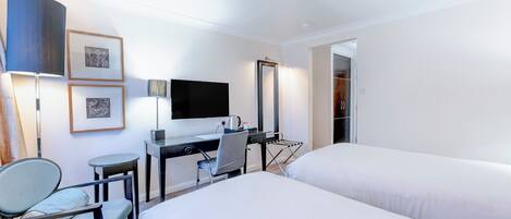Une chambre d’hôtel avec deux lits, un bureau avec un ordinateur, une chaise, une télévision et des tableaux encadrés au mur.