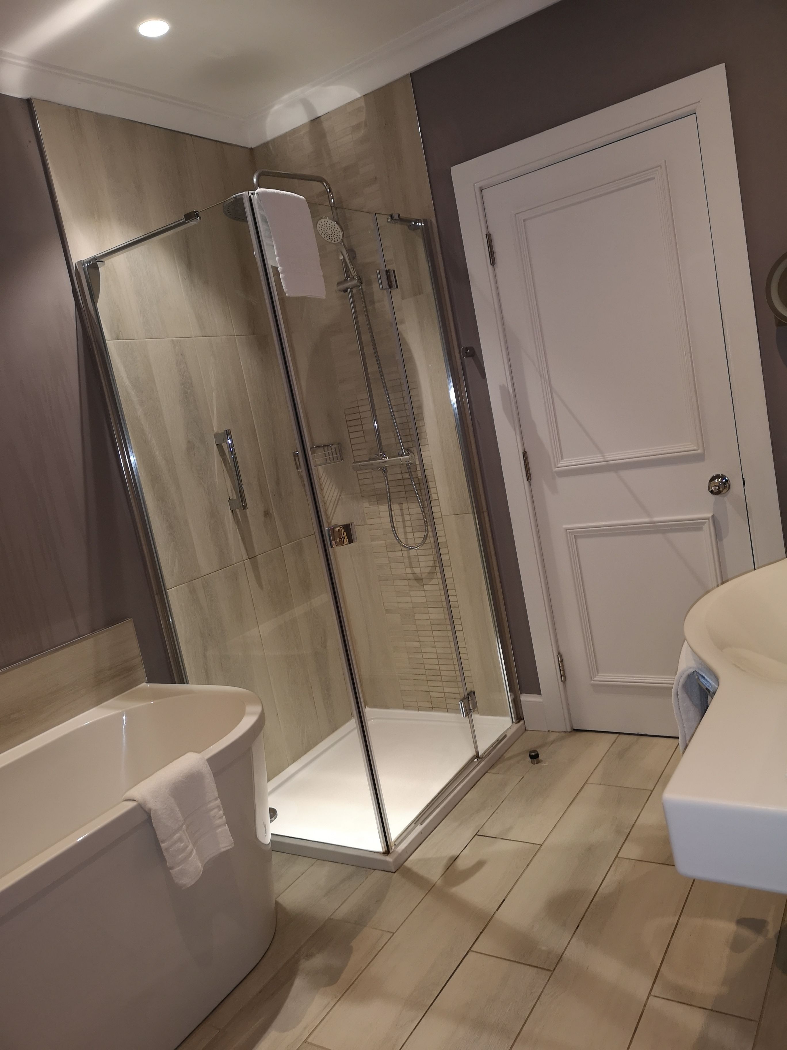 A modern bathroom with a glass-enclosed shower, a standalone bathtub, and a white door.