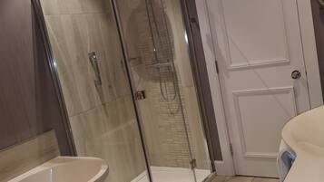 A modern bathroom with a glass-enclosed shower, a standalone bathtub, and a white door.