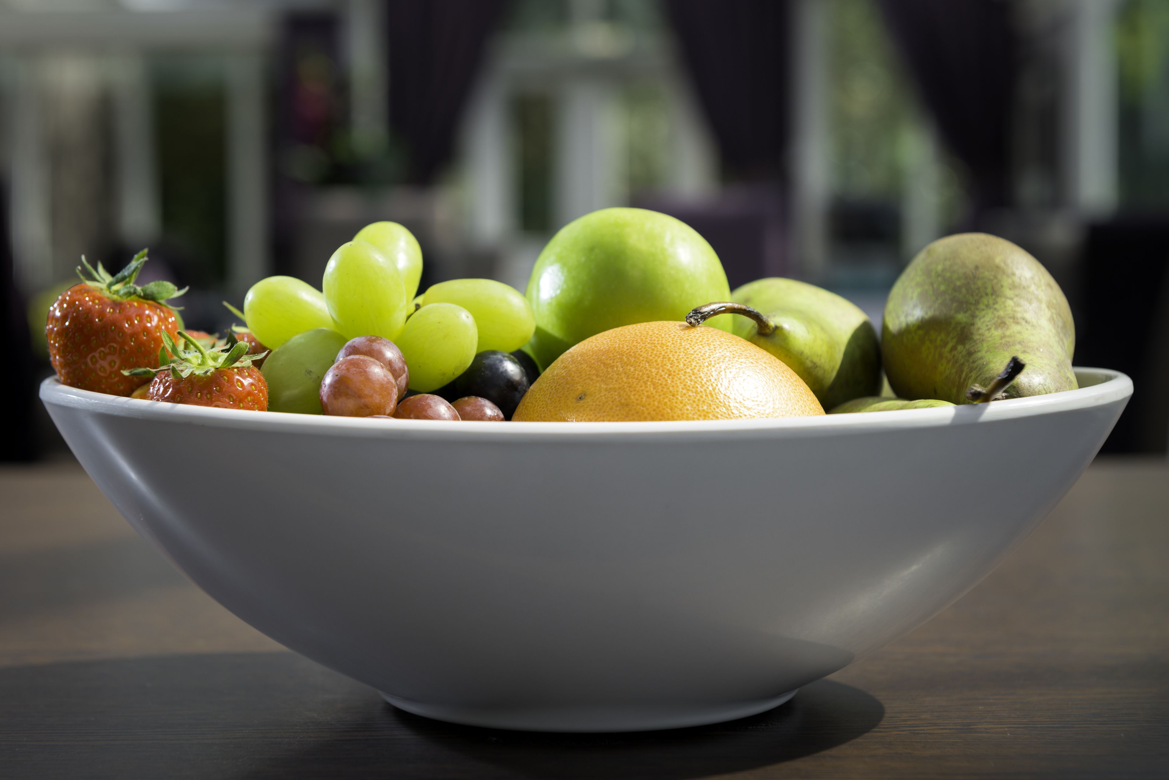Un tazón blanco lleno de frutas variadas, como uvas, manzanas y una fresa.