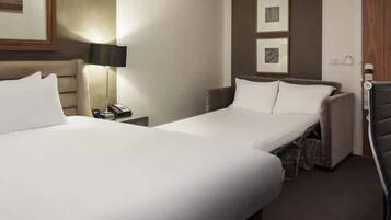 A hotel room with two beds, a desk, a lamp, and a chair.