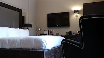Habitación de hotel con una cama grande, un televisor de pantalla plana montado en la pared, un escritorio con lámpara y una silla con detalles perlados.
