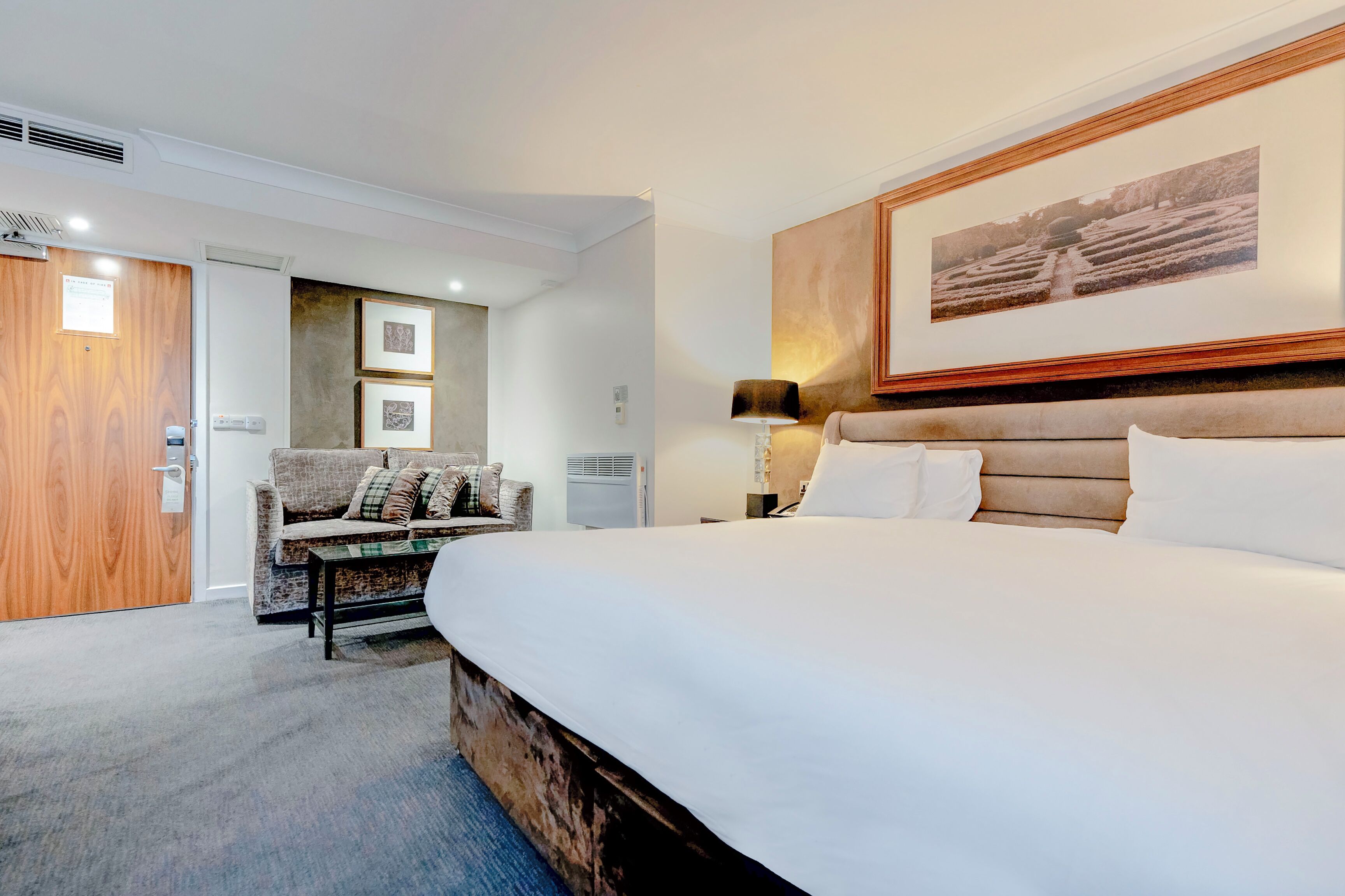 Une chambre d’hôtel avec un grand lit, une porte en bois, un canapé et un tableau encadré au mur.
