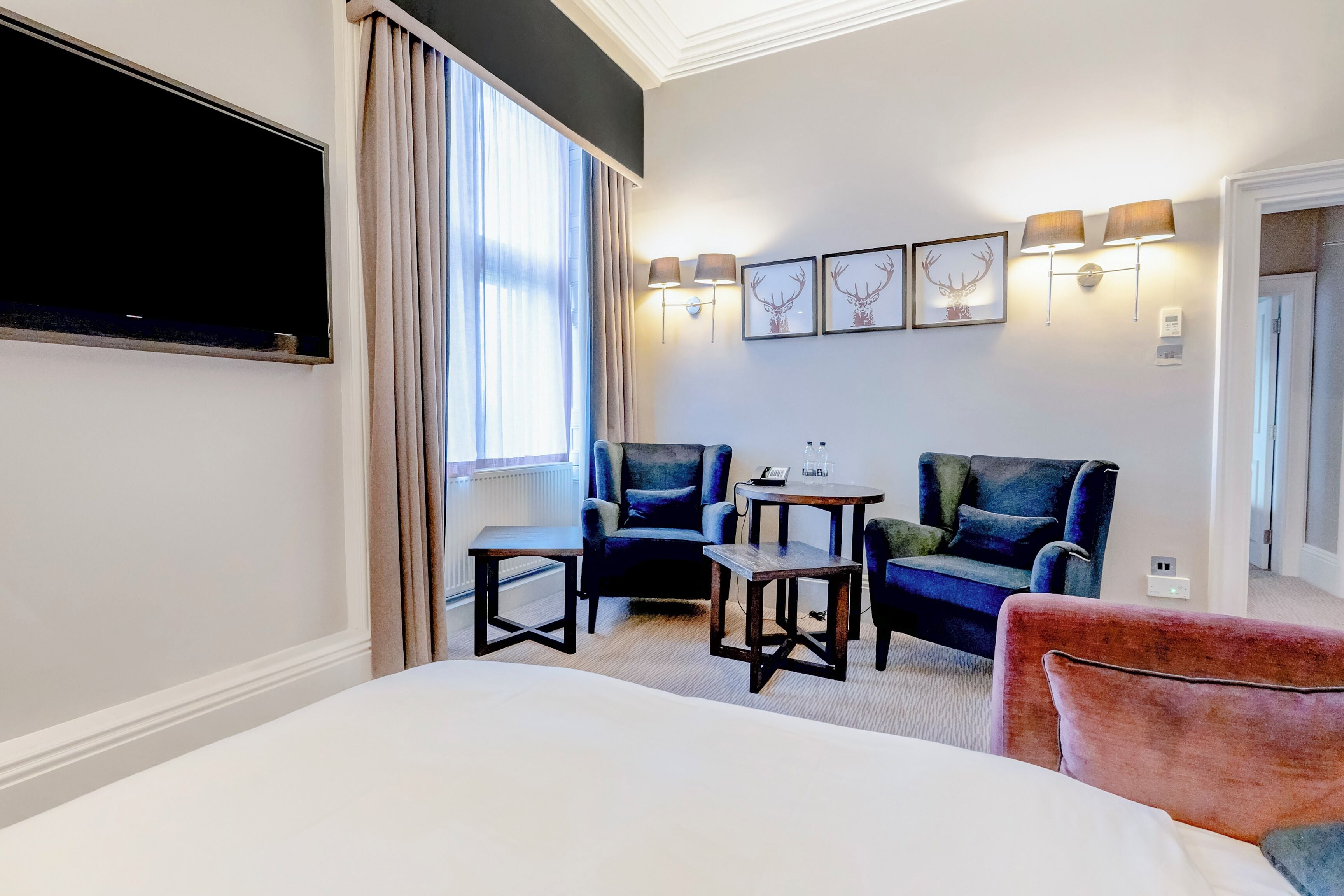 A hotel room with a bed, a TV, a seating area with chairs and tables, and artwork on the wall.
