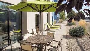 An outdoor seating area with a round table and chairs, a green umbrella, and lounge chairs along a pathway. - Springhill Suites by Marriott Billings (Billings)