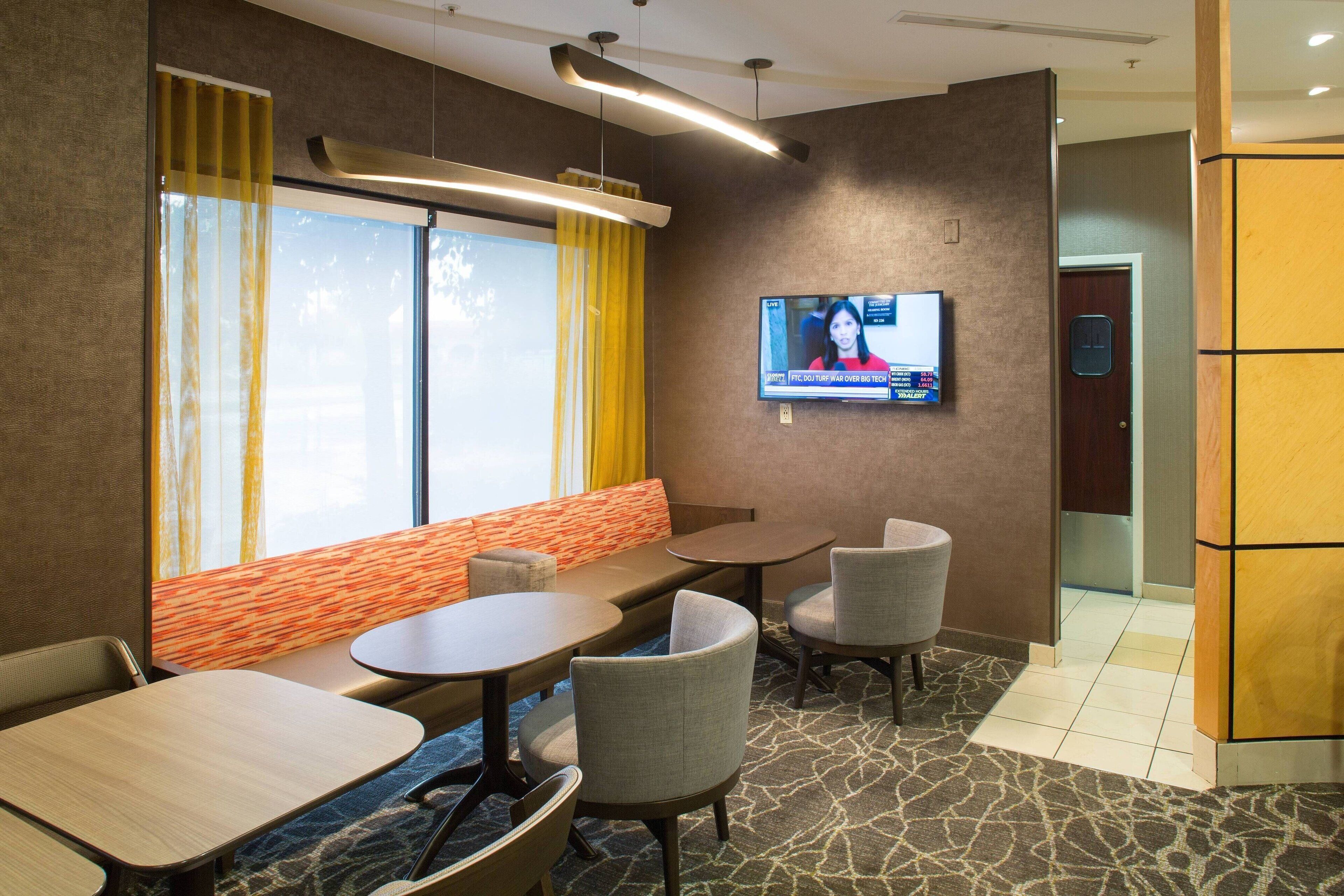 A hotel room with a seating area, a television mounted on the wall, and a door with a blue sign.