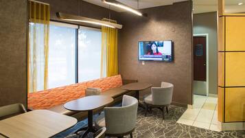 A hotel room with a seating area, a television mounted on the wall, and a door with a blue sign.