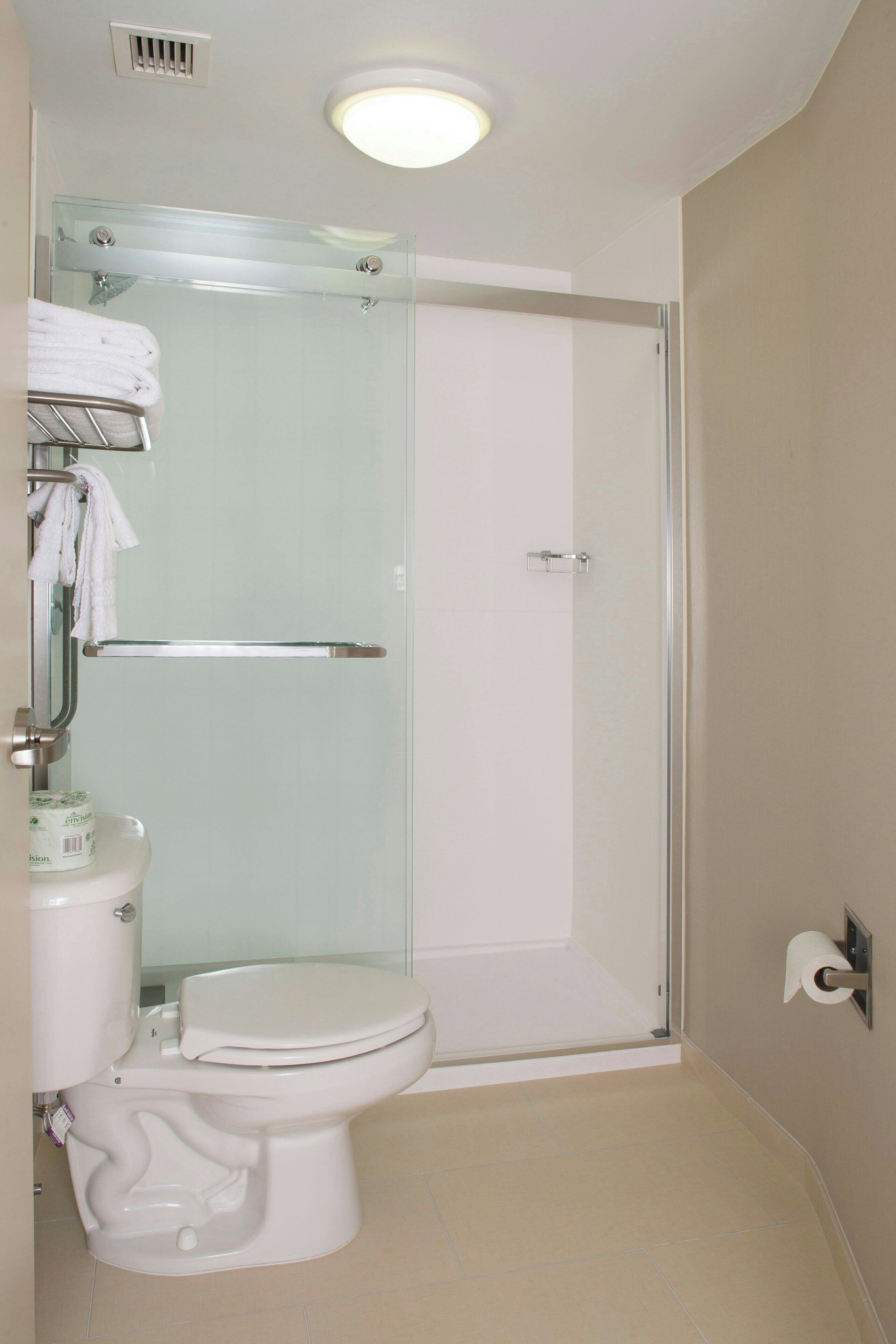 A bathroom with a glass shower enclosure, a toilet, and a towel rack with towels.