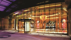 A modern building with a glass facade, a curved roof, and a central atrium with a decorative light fixture.