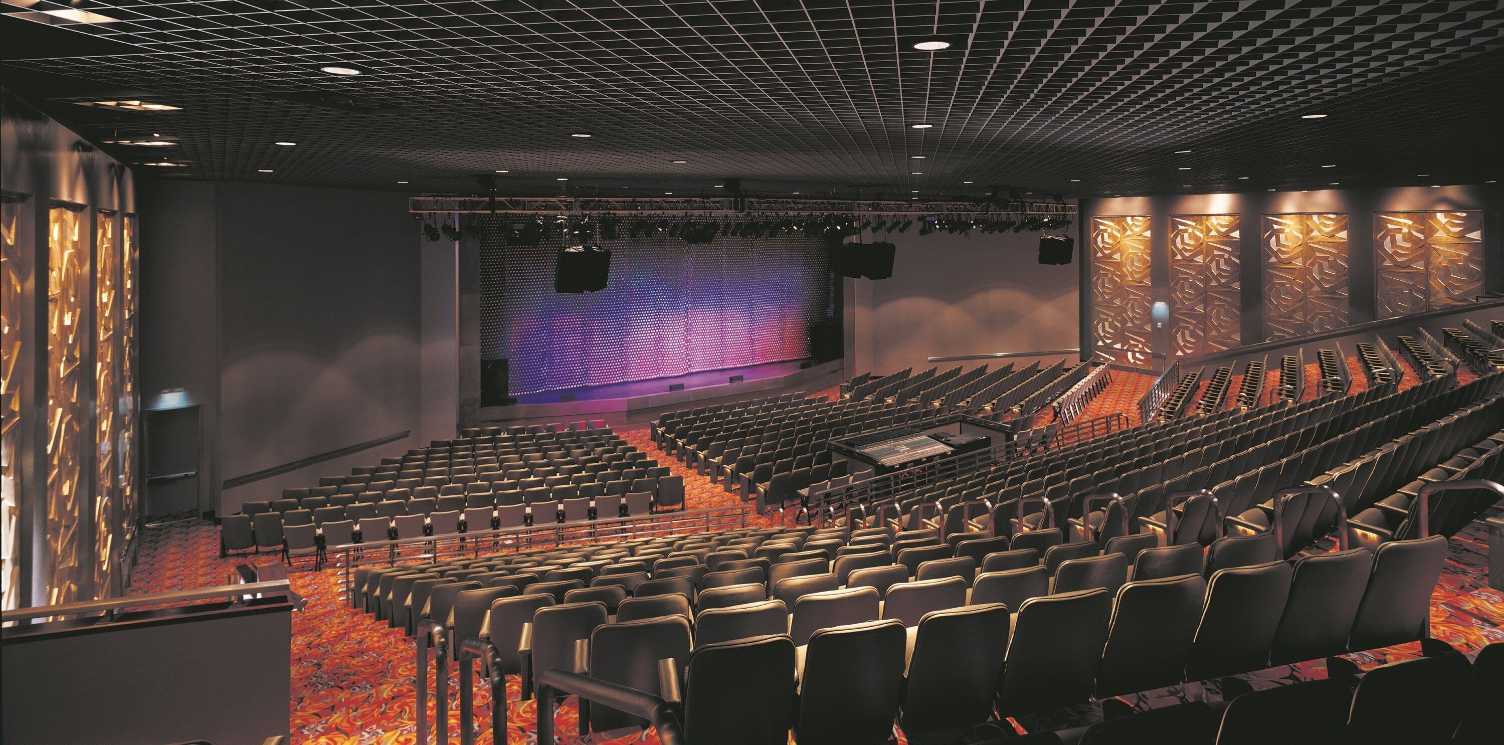 Une salle de théâtre avec des rangées de sièges, une scène dotée d’un grand écran et un mur au décor orné de motifs.