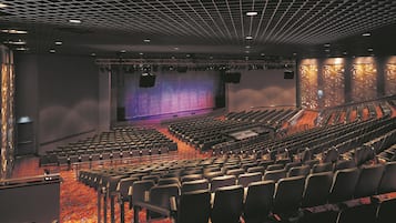 Une salle de théâtre avec des rangées de sièges, une scène dotée d’un grand écran et un mur au décor orné de motifs.
