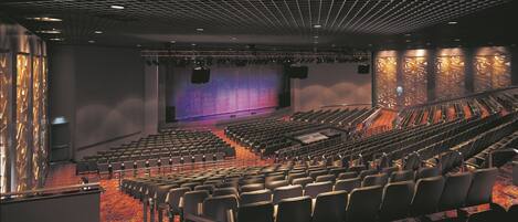 A theater with rows of seats, a stage with a large screen, and a patterned wall design.