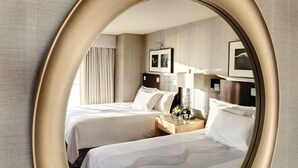 A hotel room with two beds, a nightstand, a lamp, and framed pictures on the wall.