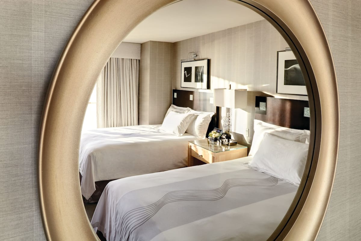 A hotel room with two beds, a nightstand, a lamp, and framed pictures on the wall.