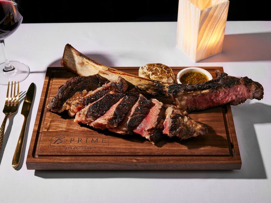 A wooden serving tray with a steak, a glass of red wine, and a candle.