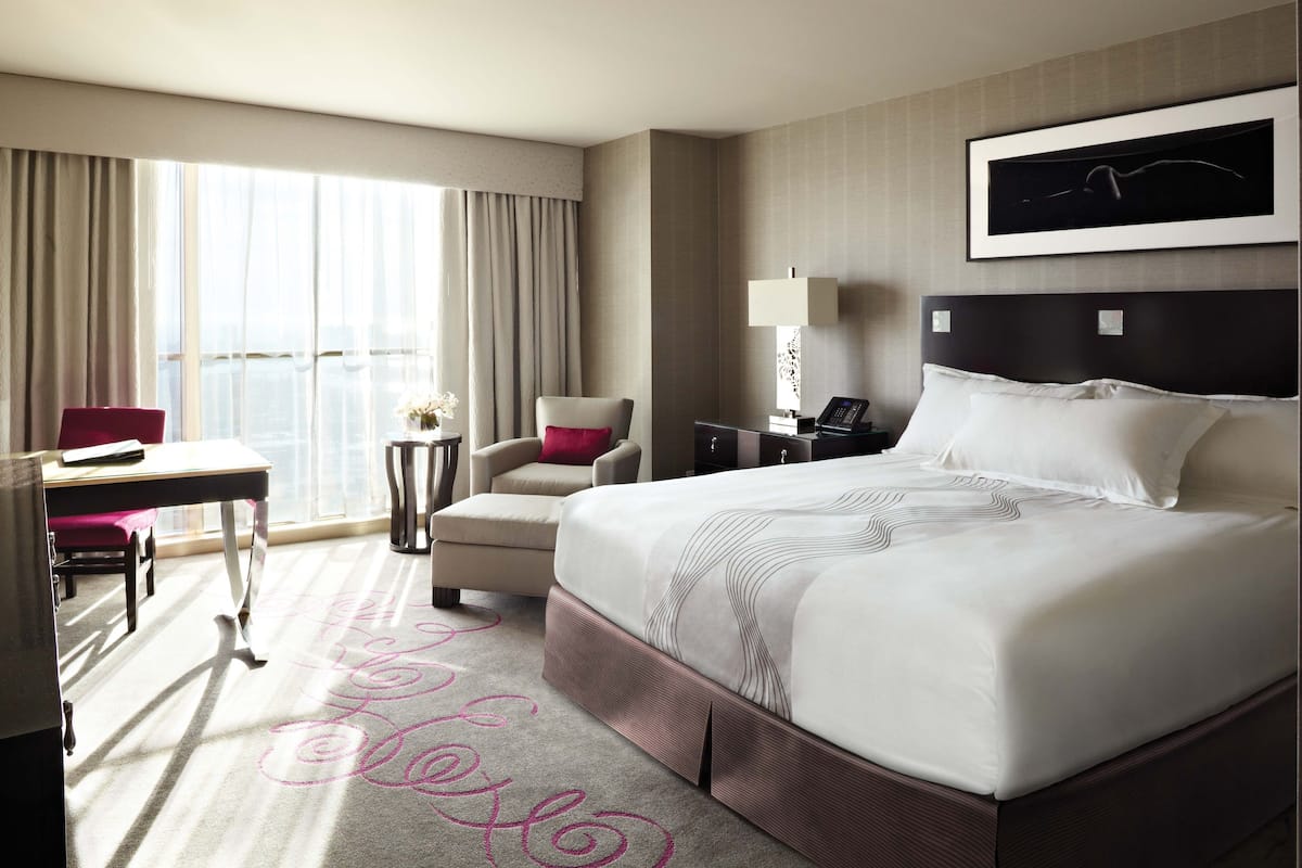 A hotel room with a large bed, a desk, a chair, a nightstand, and a window with curtains.