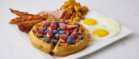 A plate with a waffle, eggs, bacon, and hash browns.