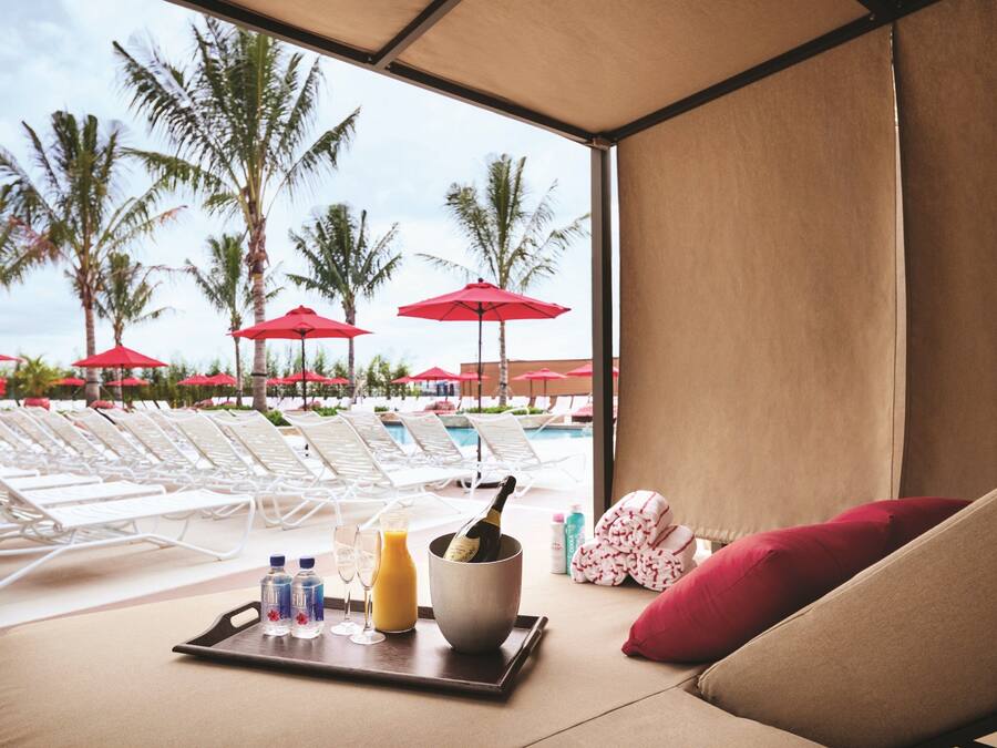 A room with a view of a pool, lounge chairs, and red umbrellas.