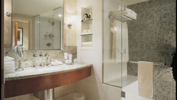A modern bathroom with a marble countertop, a large mirror, a glass-enclosed shower, and neatly folded towels.