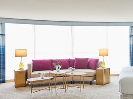 Una habitación de hotel moderna con un sofá color beige, dos mesas redondas pequeñas y dos lámparas.