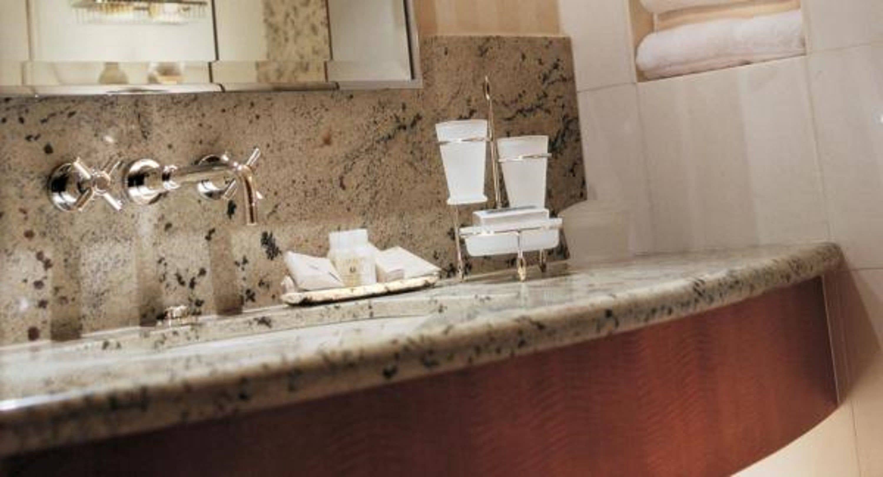 Une salle de bain avec un comptoir en granit, un lavabo avec un robinet chromé et une pile de papier toilette blanc.