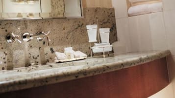 A bathroom with a granite countertop, a sink with a chrome faucet, and a stack of white toilet paper.
