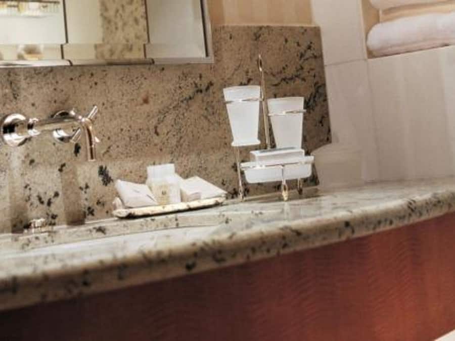 A bathroom with a granite countertop, a sink with a chrome faucet, and a stack of white toilet paper.