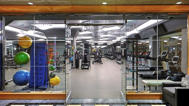 Een sportschool met trainingsapparatuur, een spiegelwand en een vloer met patroon.