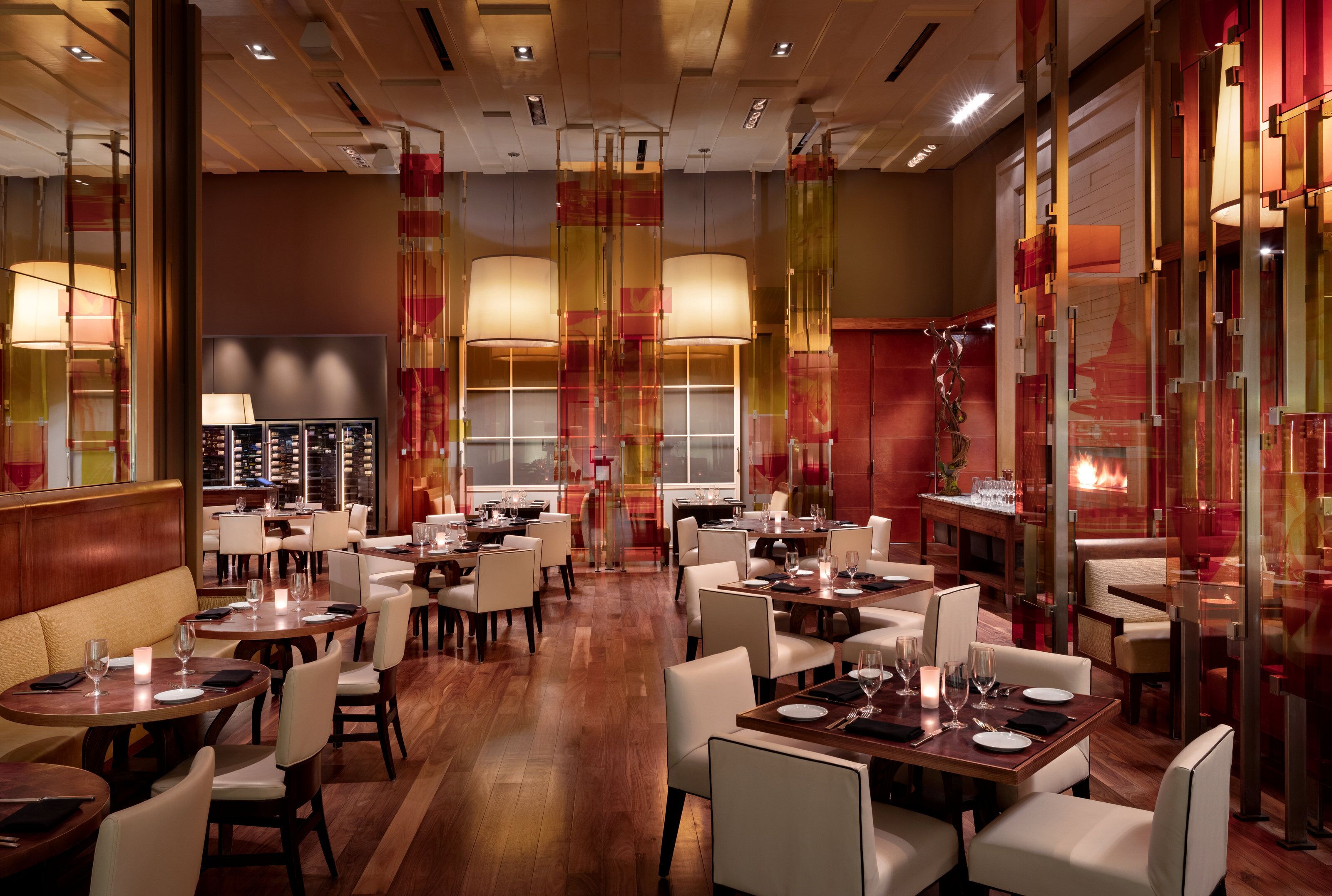 Een restaurant met meerdere eettafels en stoelen, een houten vloer en een groot raam op de achtergrond.