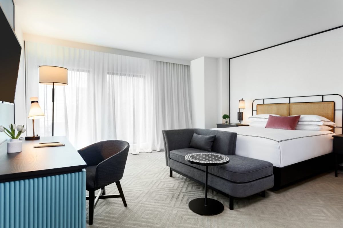 Una habitación de hotel moderna con cama, escritorio, silla, mesa redonda y mesita de noche.